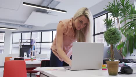 Mujer-De-Negocios-Caucásica-Usando-Una-Computadora-Portátil-Revisando-El-Papeleo-En-La-Oficina-Moderna