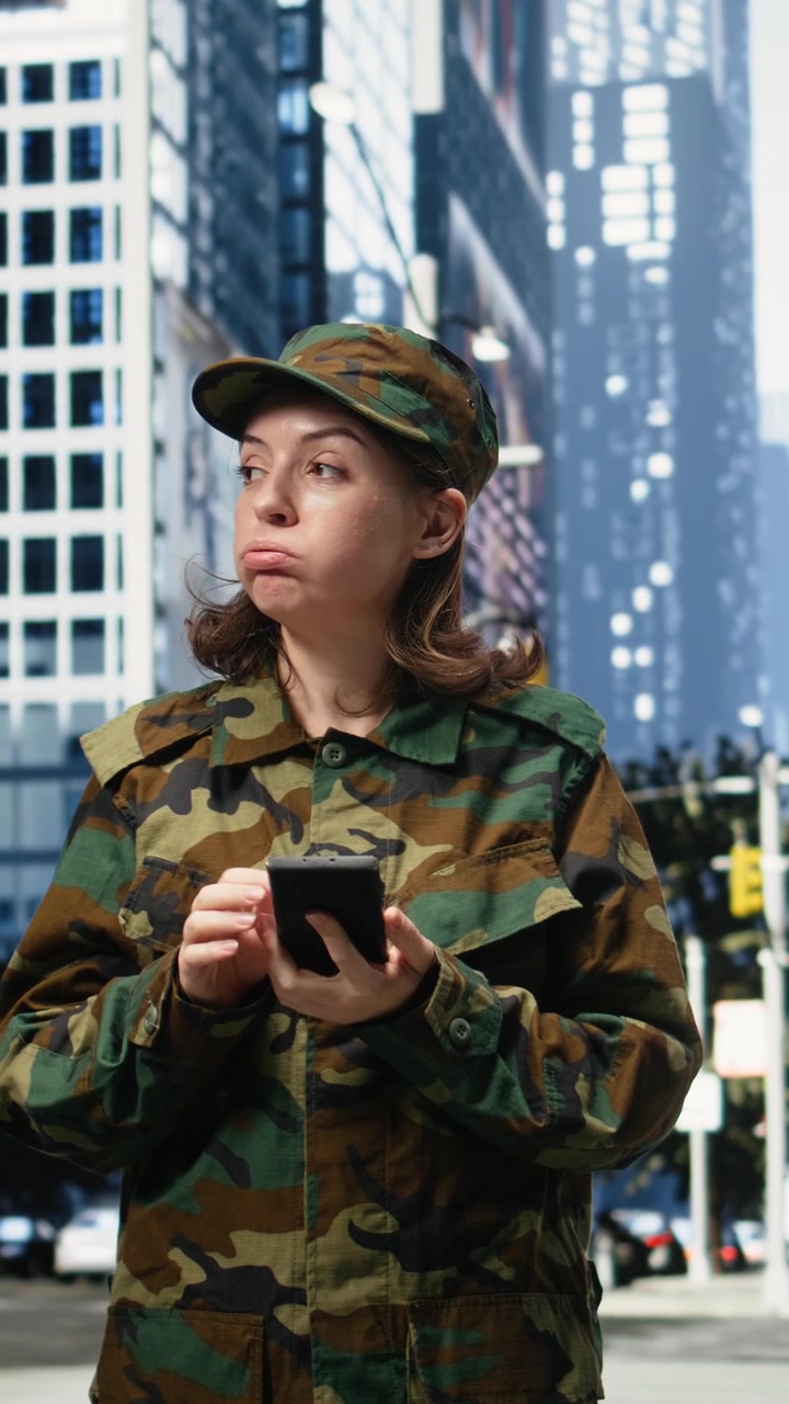Video verticale: Soldatessa imbronciata guarda lo smartphone con delusione in un quartiere cittadino