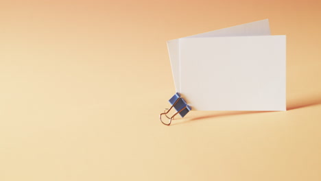 two blank white business cards with bulldog clip on orange background, copy space, slow motion