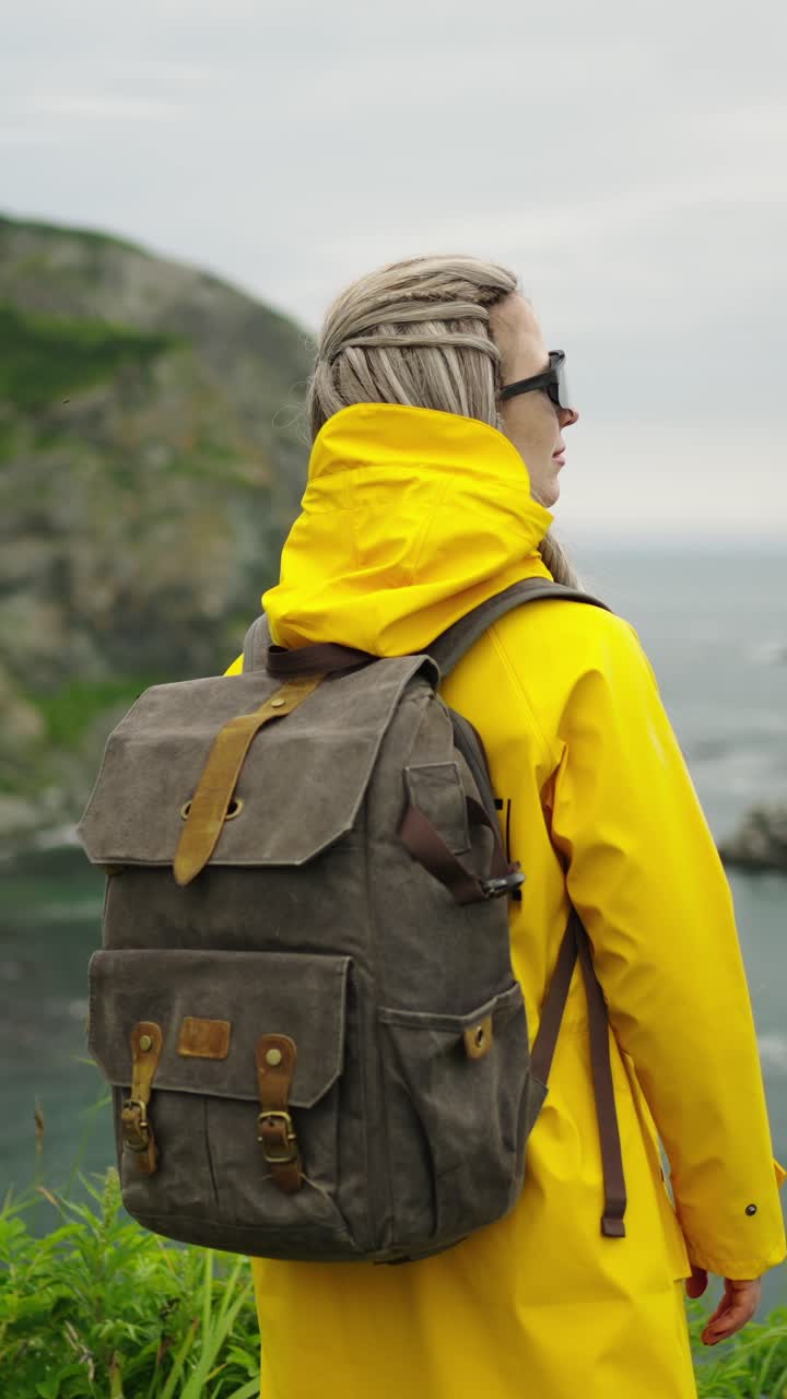 Woman in Yellow Raincoat with Backpack Looking at Ocean View