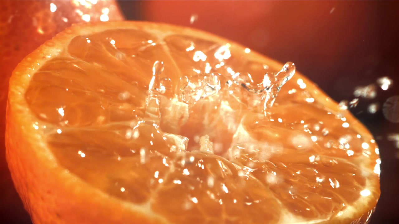 Zeitlupe: Wassertropfen spritzen auf eine frische Orangenhälfte