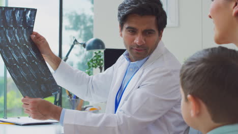 Doctor-In-White-Coat-With-Mother-And-Son-In-Office-Looking-At-MRI-Or-CT-Scans