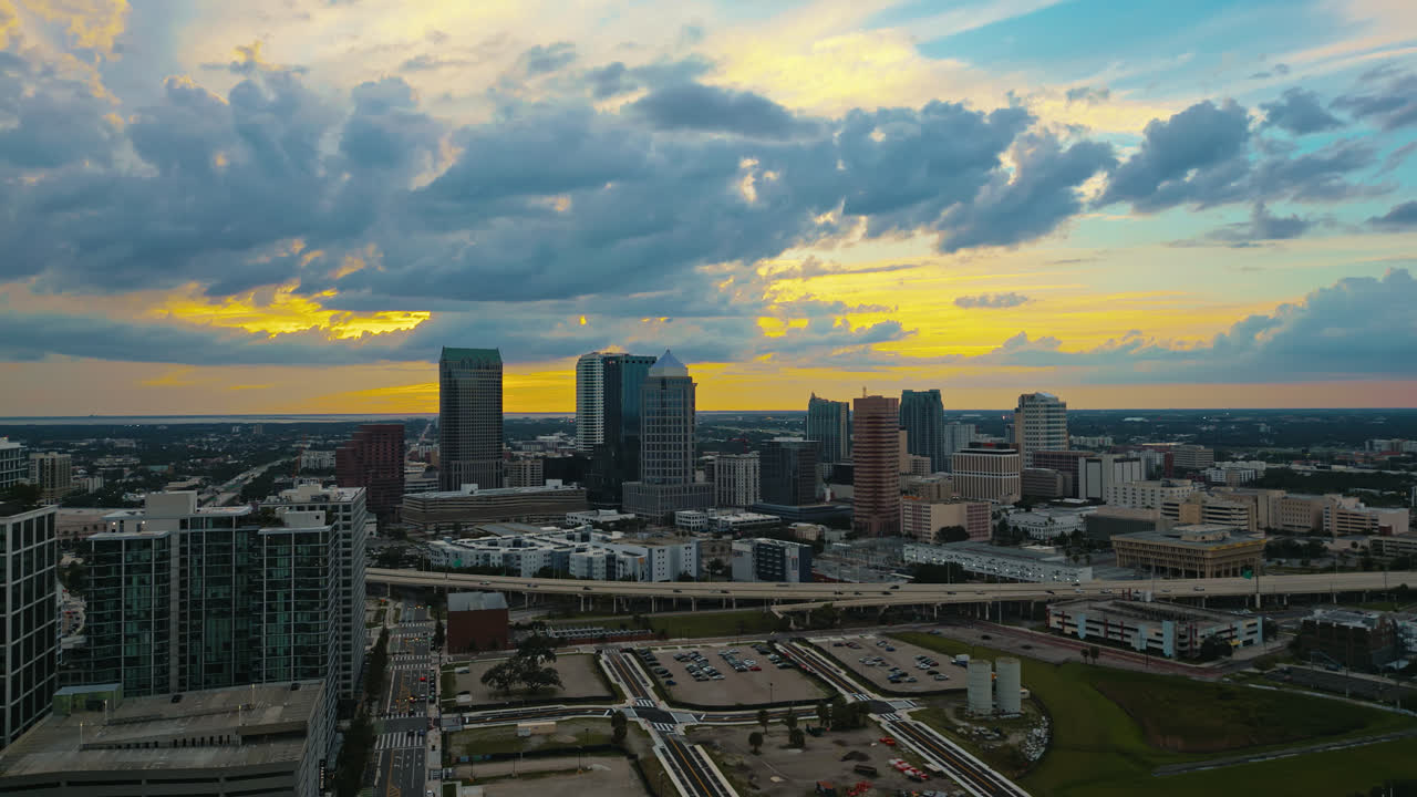 Tampa downtown skyscrapers and city blocks with an orange glow in sky as the sun is just starting to set, aerial tracking left