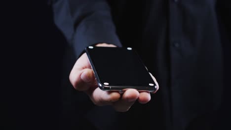 hand of a caucasian man wearing a black shirt cradling a smartphone