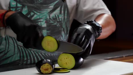 chef cocina rebanar cortar berenjena on tabla de cortar con guantes negros