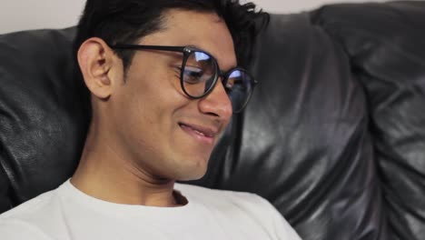 young man with glasses sitting on couch and smiling, close up view