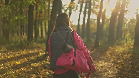 woman walking in autumn park with yoga mat