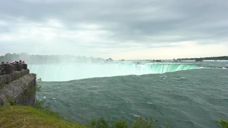 niagara falls landscape view over water flowing down the waterfall creating steam, on a cloudy day