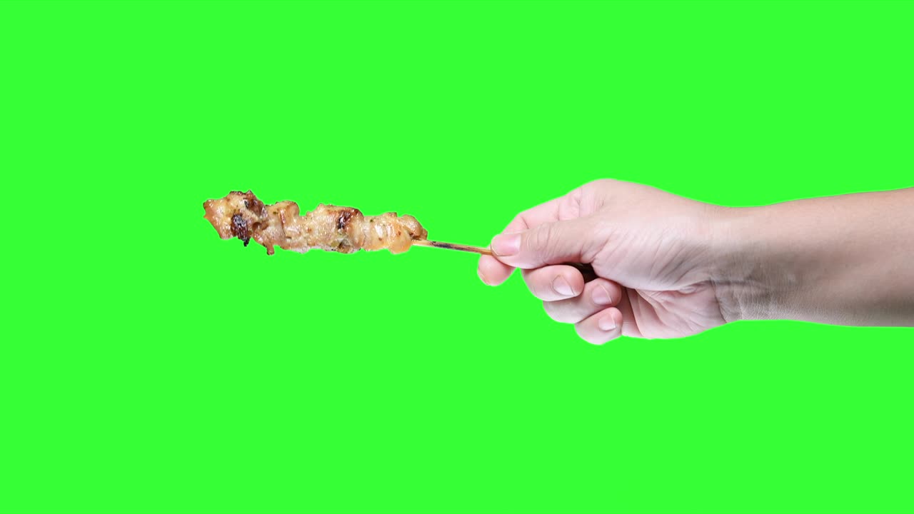 초록색 스크린 배경에 바베큐 사타이 을 들고 있는 손.