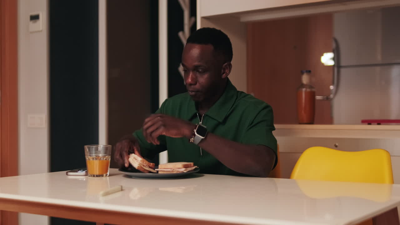 Young Man Eating a Sandwich and Drinking Juice in a Modern Kitchen