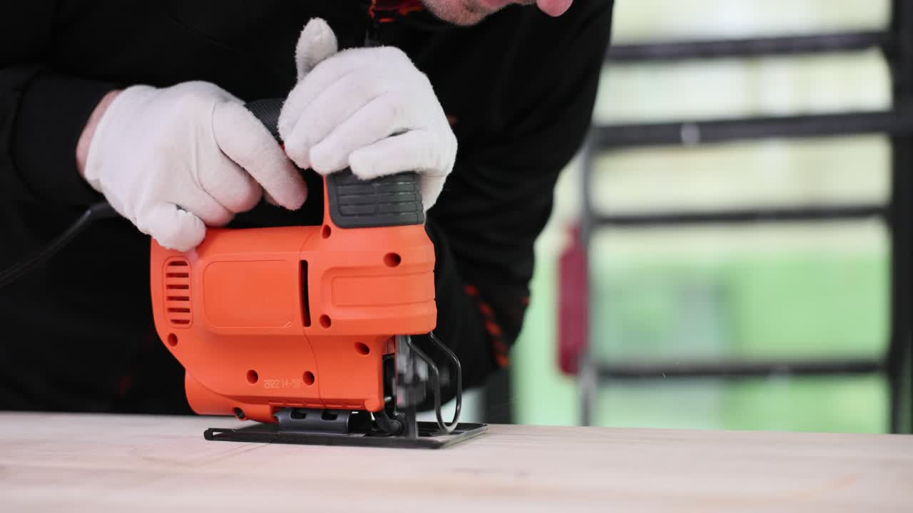作業員が工房で手持ちのジグソー工具を使って木製の板を切断している。