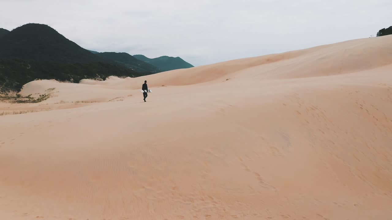 sandboarder caminando sobre dunas de arena cerca de la playa tropical de garopaba, santa catarina, brasil