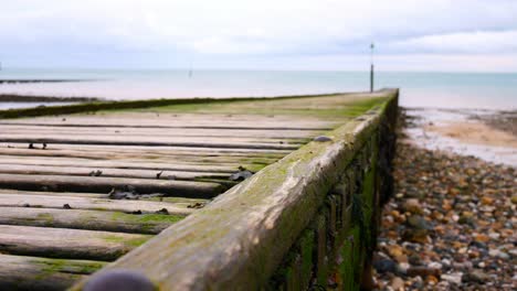 Weathered-wooden-boardwalk-jetty-leading-towards-calm-overcast-ocean-dolly-right