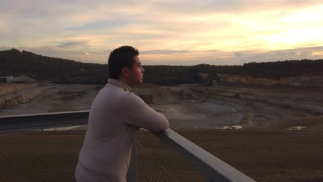 un joven con un suéter de cuello alto mirando la cantera mientras se pone el sol