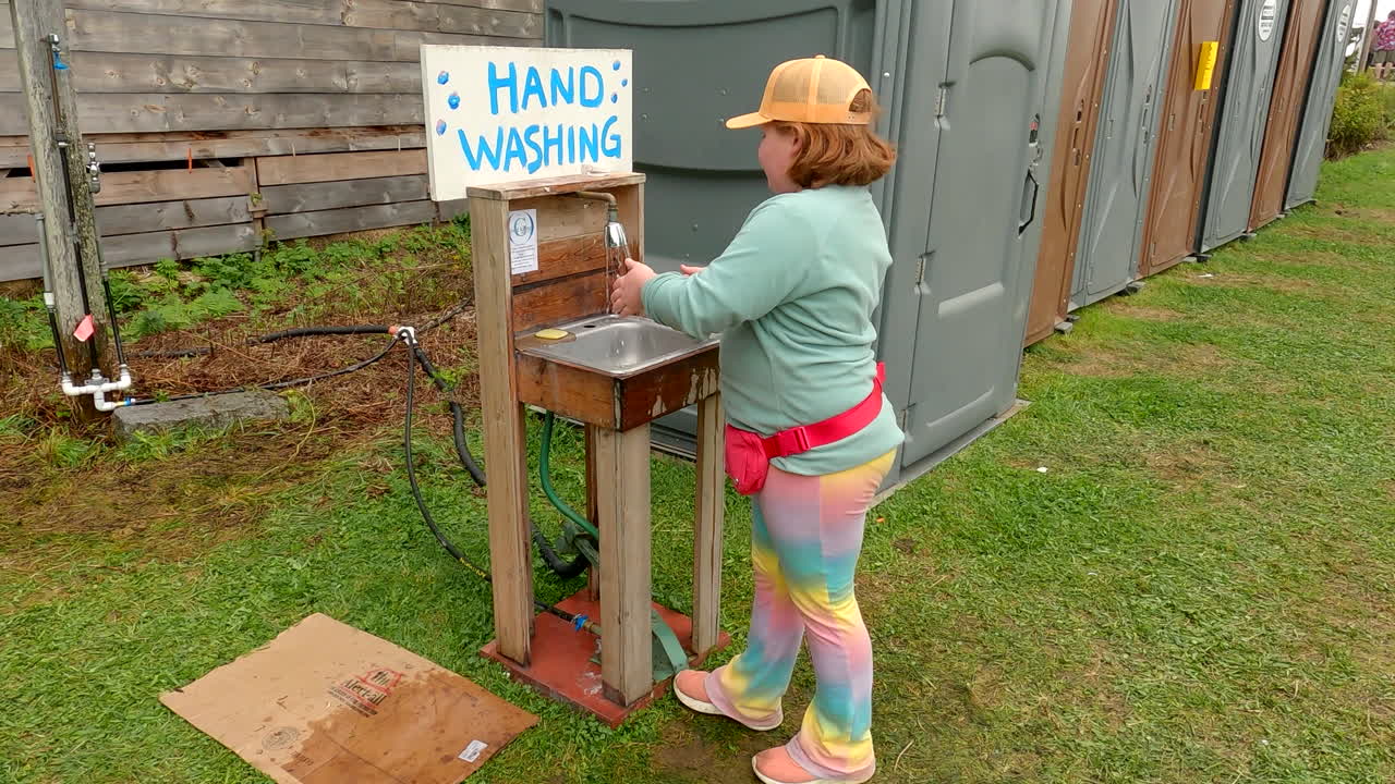 Young Girl practices good hygiene by washing hands after using the portable toilets at a festival, ensuring cleanliness and safety by utilising the soap and water provided