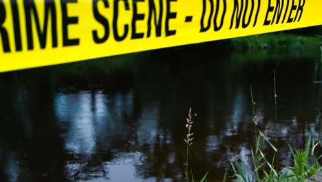 gorgeous vibrant colored yellow crime scene do not enter tape in frong of a rainy lake where rain drops fall in slow motion on the water surface creating water ripples and small waves. eerie day time