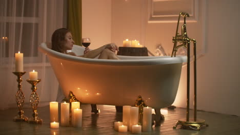 woman bathing with pleasure lying down in the tub with foam and drinking red wine spending time in luxury spa resort