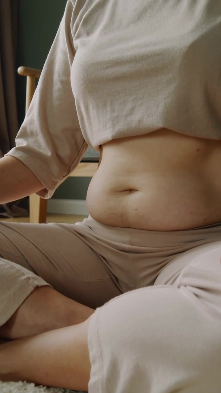 Video verticale: Donna che si sistema su un tappeto, si muove, solleva il busto e si siede dritta, indossando abbigliamento da casa beige.