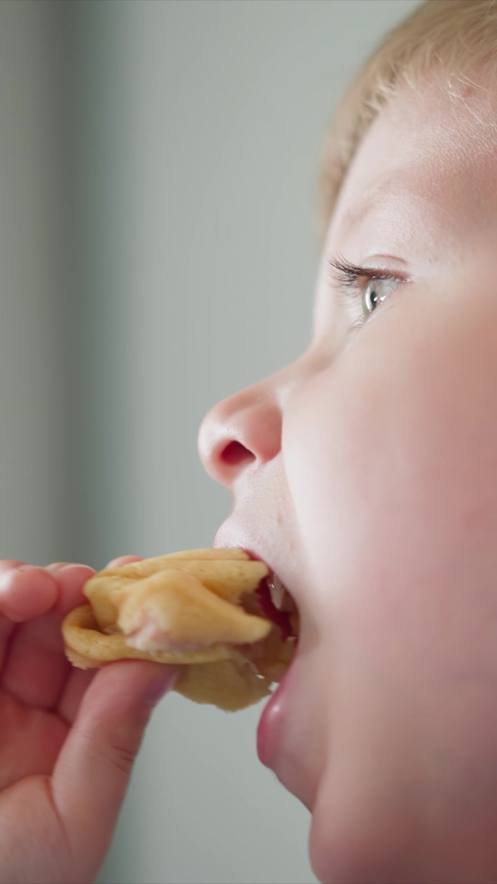 Close up of young boy eating food with his hand visible. sequence shows progression of him taking bites from small pieces focusing on facial expressions and mouth movements against plain