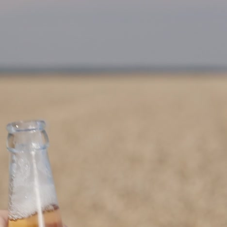 Men's-hand-opens-a-bottle-of-beer-against-the-background-of-the-field-where-wheat-grows