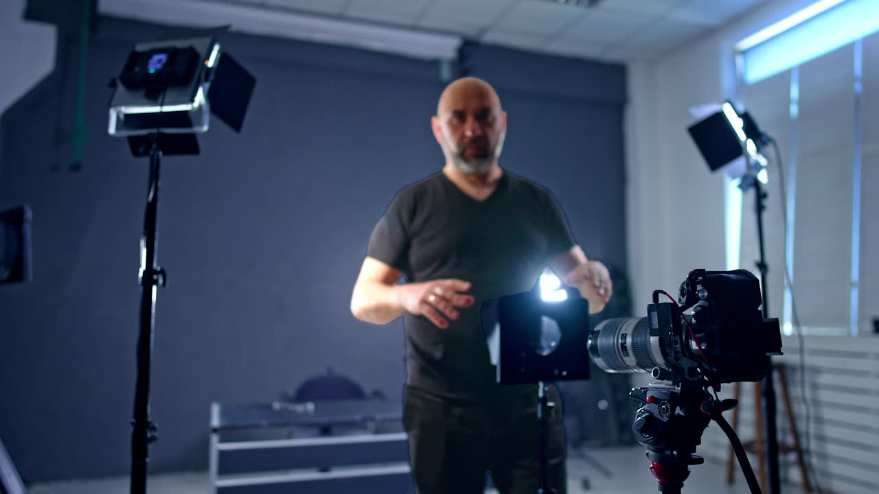 Bald Caucasian man wearing black clothes sets lens in front of camera. Photographer arranging equipment for shooting in studio.