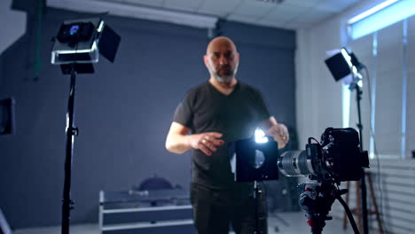 bald caucasian man wearing black clothes sets lens in front of camera. photographer arranging equipment for shooting in studio.