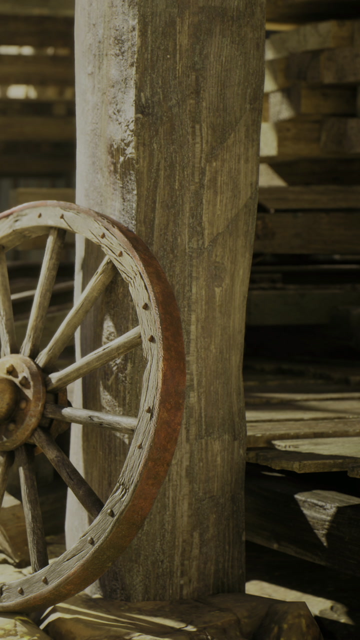 Rustic wooden wheel resting against a weathered post in a sunlit barn