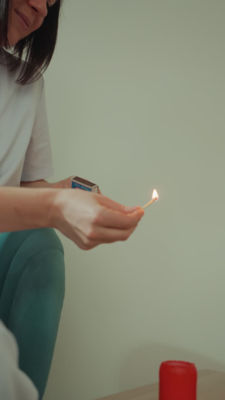 Estetista caucasica accende candele rosse da spa, prepara un massaggio facciale a microcorrente con movimenti delicati delle mani, primo piano dell'accensione di un fiammifero, bagliore caldo della fiamma, ambiente clinico accogliente e calma professionale.