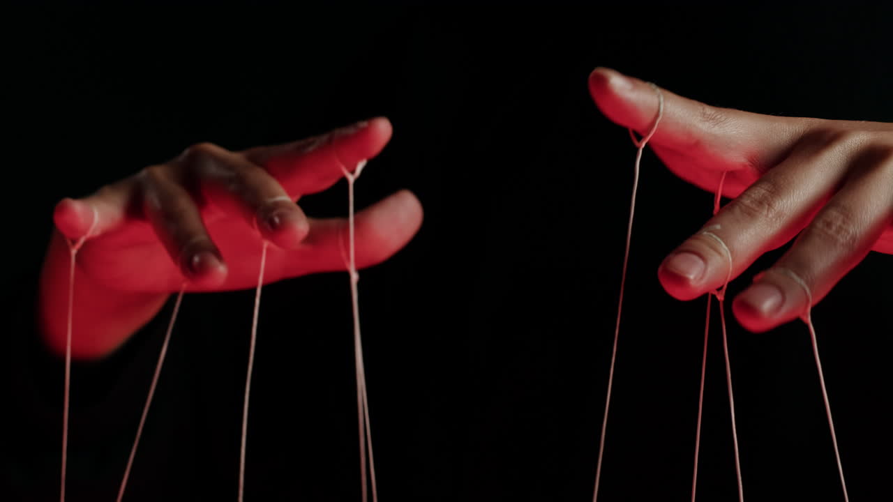 Close-up of Hands Manipulating Puppet Strings Under Red Light