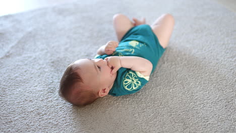 lovely infant child lies on the floor holding his fingers in mouth. little calm baby looks into camera over his head.