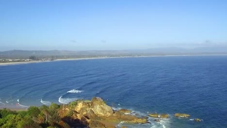 Aerial-drone-travelling-shot-approaching-Byron-Bay,-over-beach-lookout