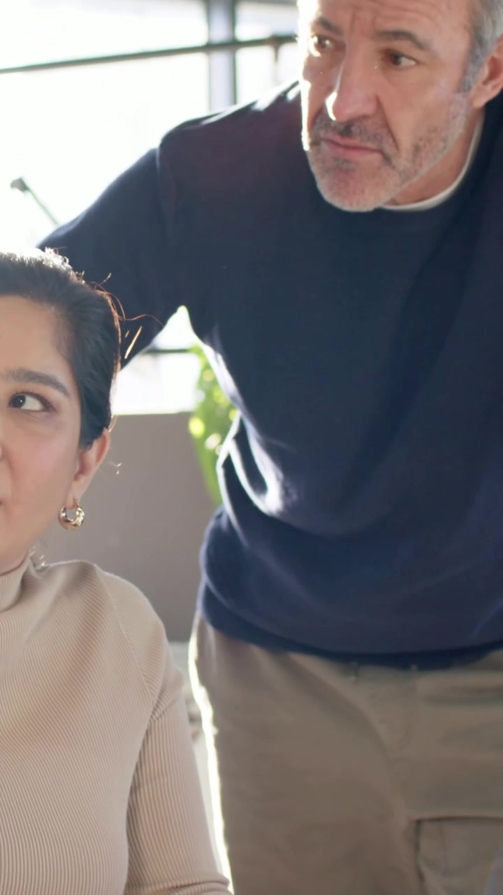 Video verticale: Uomo che si avvicina e guida una donna con un top color cuoio e orecchini a cerchio dorati, che guarda vicino alla finestra, pianta