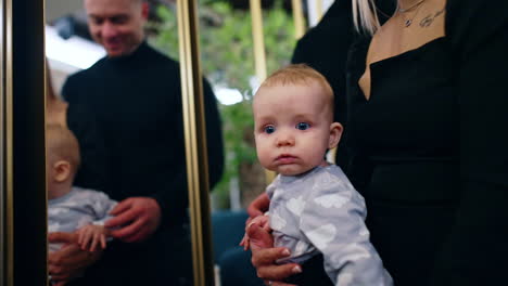 beautiful caucasian family of three in the room with mirrors. camera approaches the infant kid with big blue eyes.