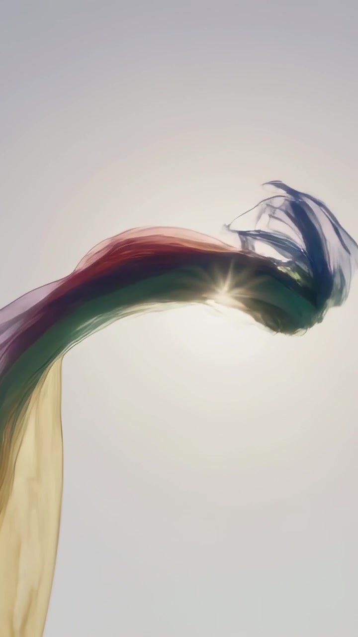 Vertical video: Waving colorful thin scarf arcing across blue sky, gust lifting colors to catch sun