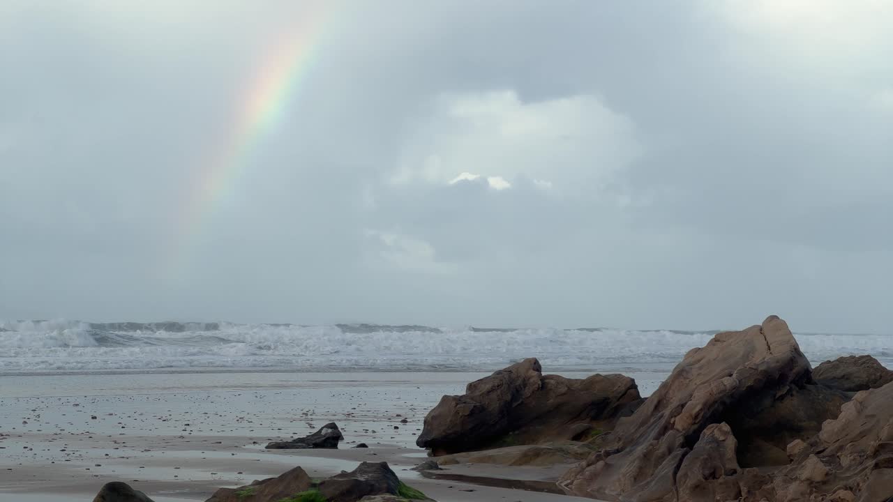 un arco iris adorna el cielo sobre las olas del mar que se estrellan contra la escarpada y rocosa costa de zahara, españa, encarnando el atractivo y las maravillas naturales del paisaje costero.