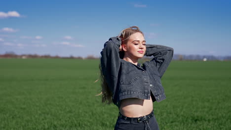 beautiful girl on field at sunlight. young woman in denim suit standing with closed eyes to the sun. attractive model outdoors.