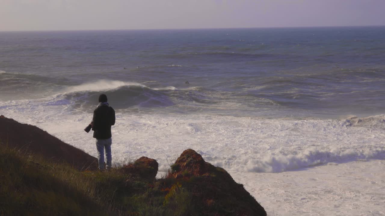 fotógrafo en la cima de un acantilado con grandes olas en el fondo