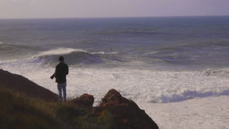 Fotógrafo-En-La-Cima-De-Un-Acantilado-Con-Grandes-Olas-En-El-Fondo