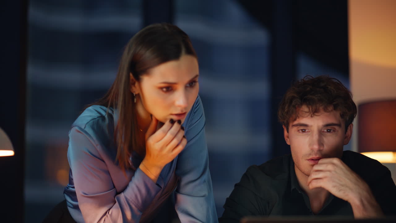 Frustrated coworkers looking computer at dark workplace closeup. Two managers