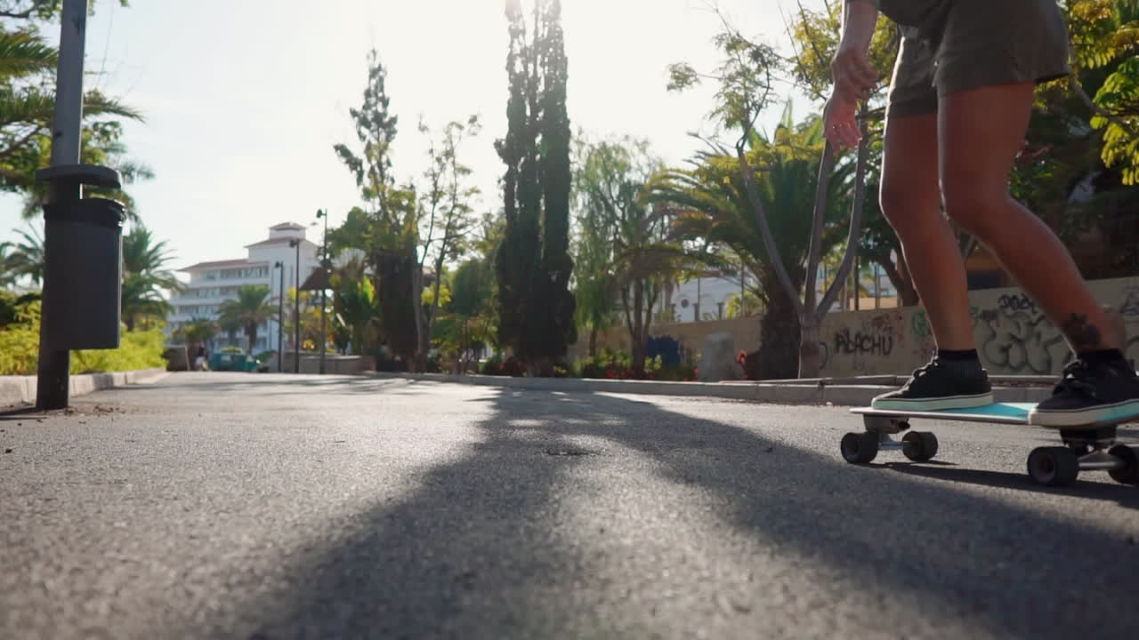 With palm trees as a backdrop, slow motion reveals a young woman cruising on a longboard in the summer, wearing shorts and sneakers