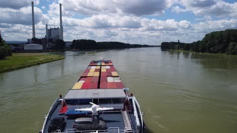 beautiful drone shot over rhine river in germany with coal power plant on left shore while camera is stationary and a long loaded cargo ship is pushing forward on the river