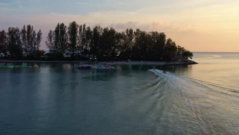 Aerial-shot-drone-flyover-capturing-water-sport-activity,-banana-boat-ride-pulling-behind-a-jet-ski-at-sunset,-Langkawi-island