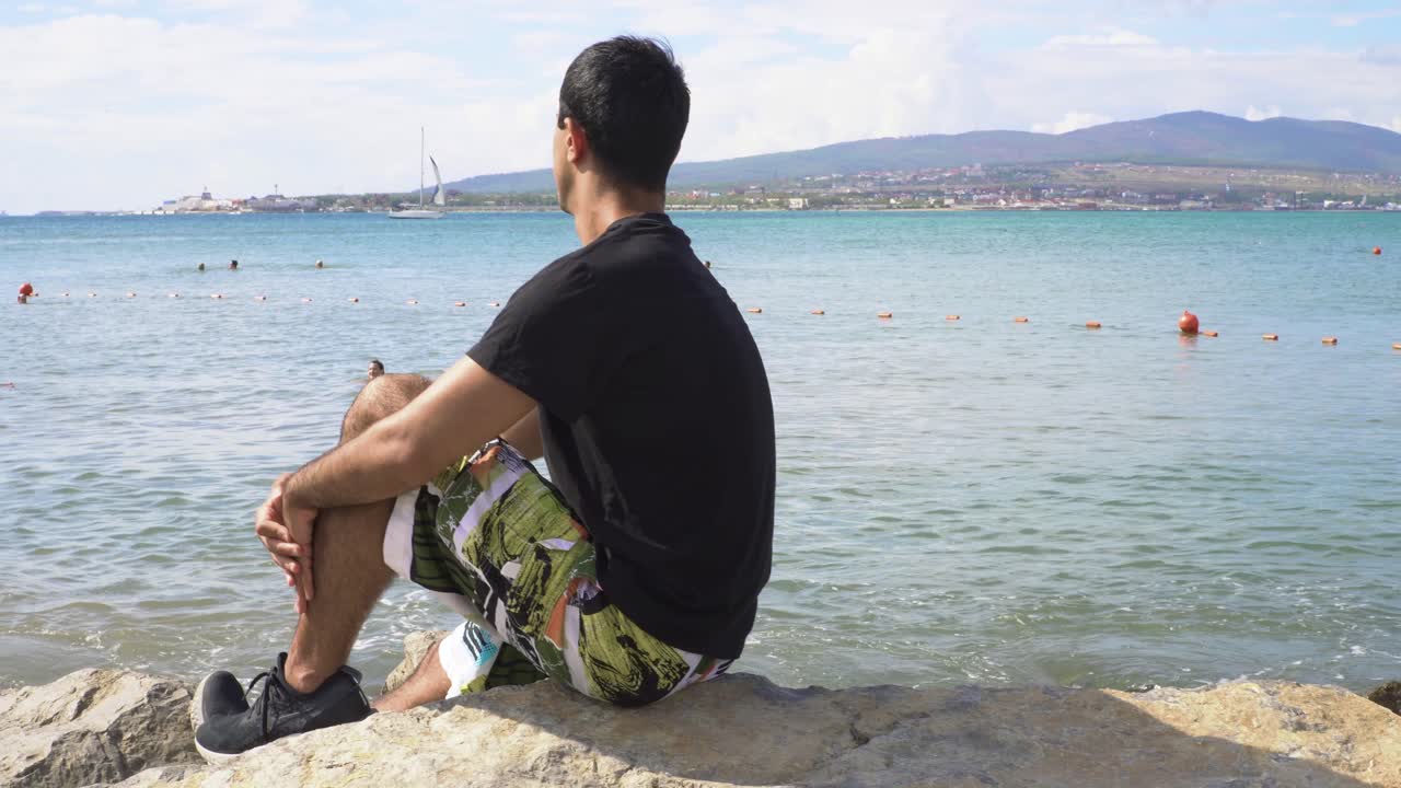 hombre sentado en la playa mirando el océano