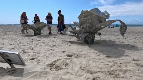 people observing a beach sculpture