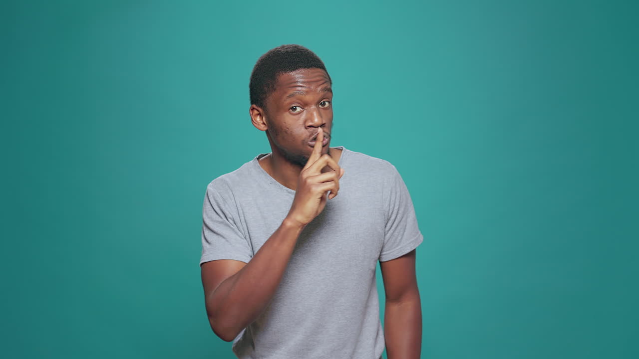 Portrait of secretive man doing hush sign in front of camera