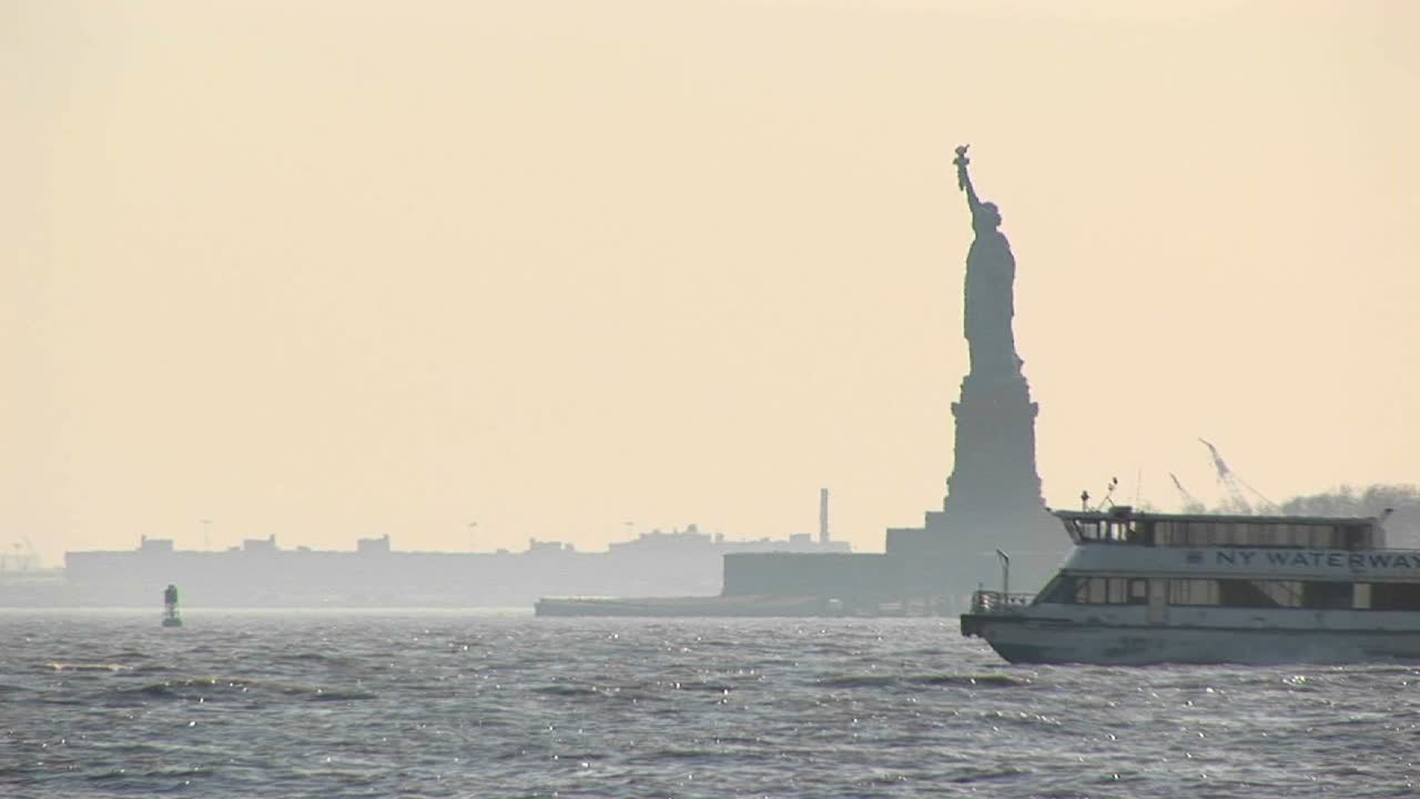 여객 페리는 백그라운드에서 자유의 여신상과 함께 뉴욕 항구에서 서로를 통과합니다.