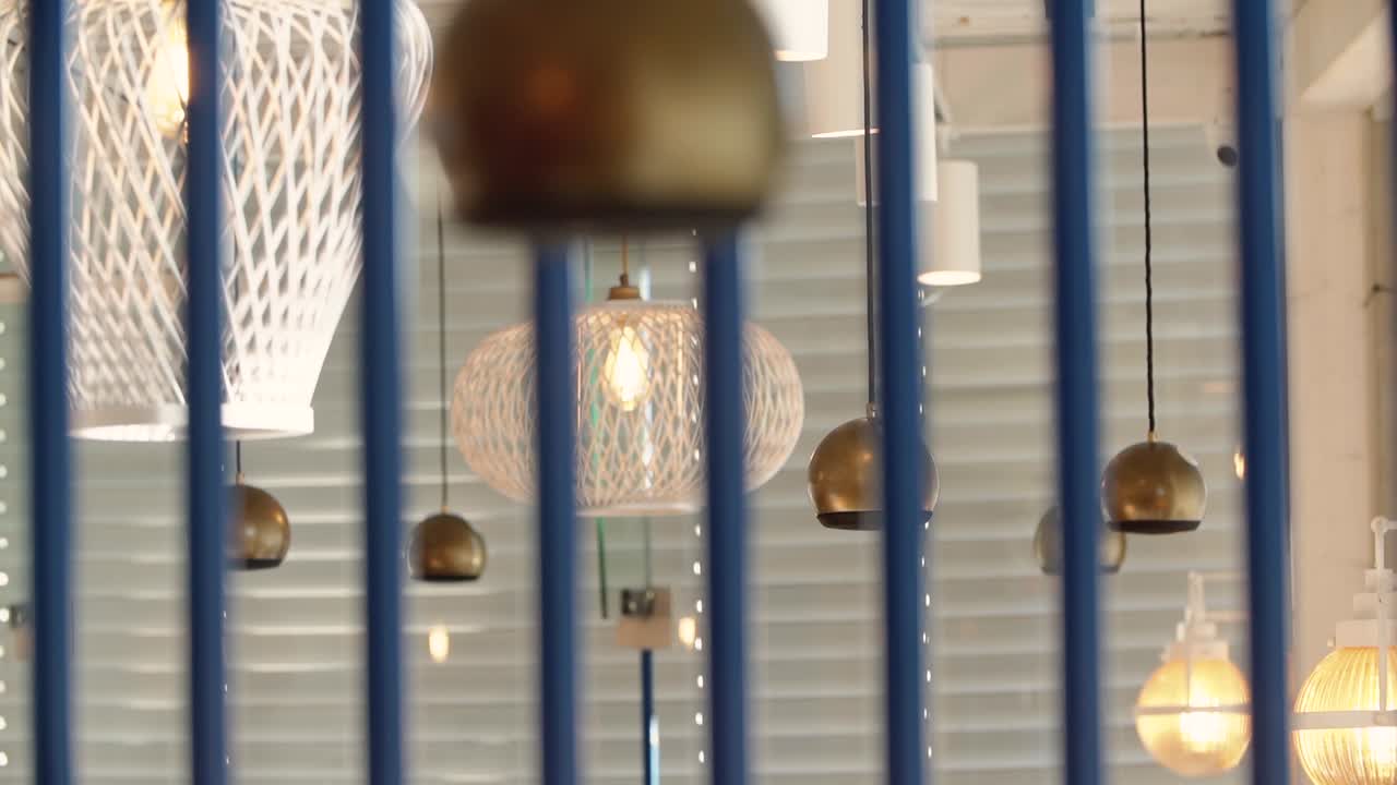 Warm and stylish coffee shop interior with modern pendant lights, geometric lamp shades, viewed through blue railing details creating artistic depth and cozy café ambience