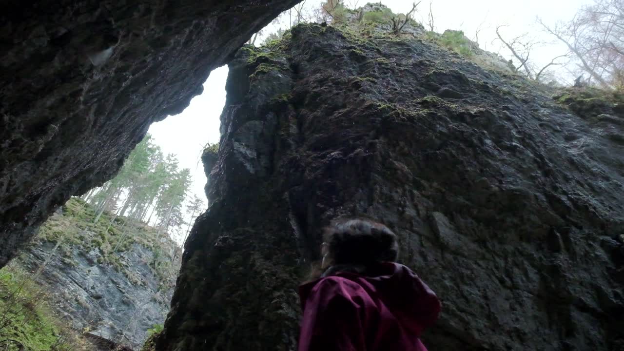 Slow-motion of water falling down from the top of the gorge. Lady standing looking up at the water falling during winter. Pokljuka Gorge in Slovenia Triglav National Park