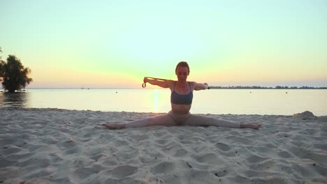 stretching outdoors. fitness elastic band. athletic young woman is doing exercises using fitness elastic band, at the beach during sunset or sunrise. fitness training outdoors. doing sports in the morning. fitness, sport, yoga and healthy lifestyle