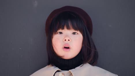 korean girl in a gray coat and cap stands the street in spring at the glass doors of the store